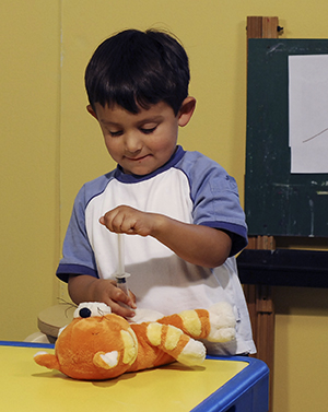 Niño que juega con una jeringa de juguete y un osito de peluche.